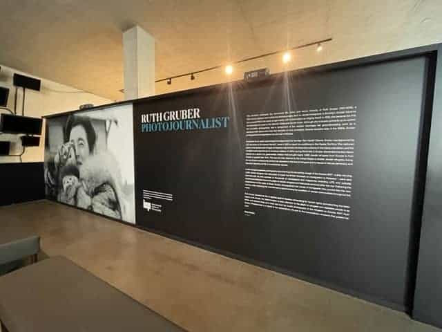 A stunning exhibit display features a large black and white photo of a woman holding a camera, achieved through large format printing. Text on the right reads 