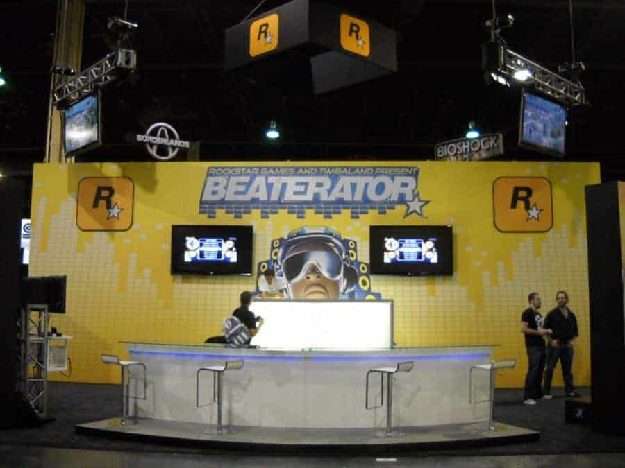A booth at an event features a large yellow backdrop with 