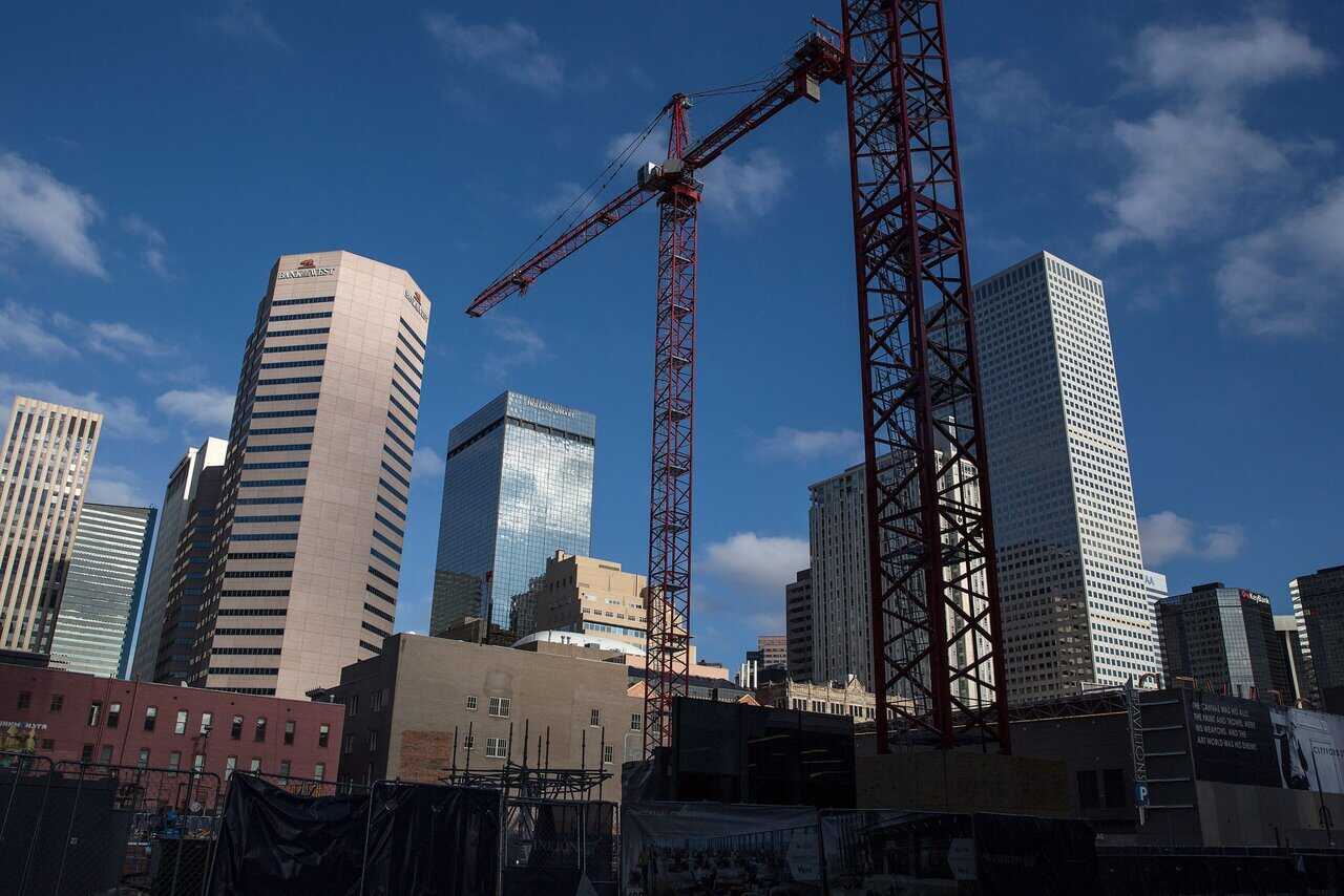 Tall red construction cranes stand in front of modern skyscrapers under a blue sky with scattered clouds. The cranes mark active Service Areas on the building site, while the city skyline features glass and concrete high-rise buildings.