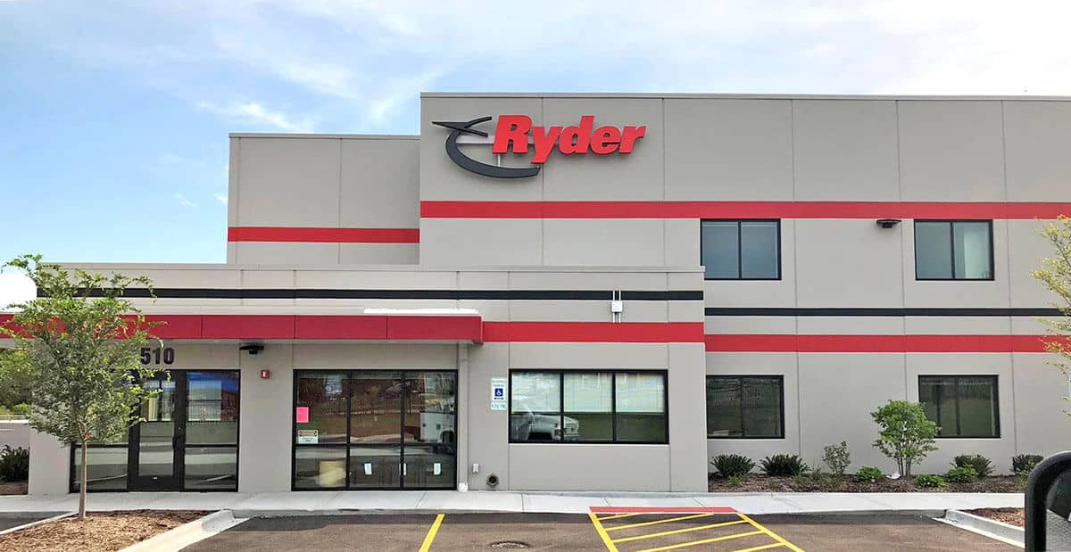 A modern Ryder building in Los Angeles with gray walls, red and black stripes, large windows, and the Ryder logo featured on outdoor signs above the entrance. Accessible parking, a sidewalk, and small trees sit in front under a mostly clear sky.